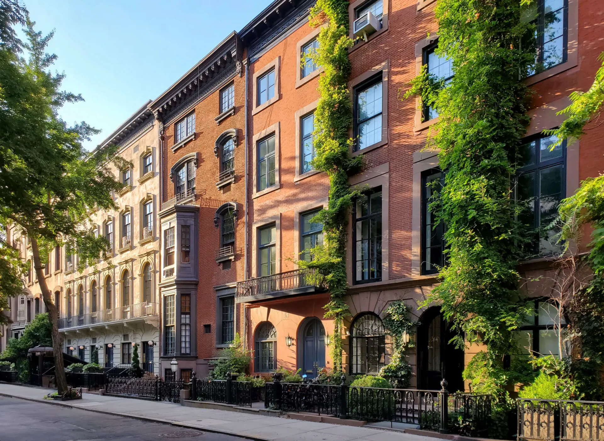 Tree-lined street with charming brick townhouses and ivy-covered facades.