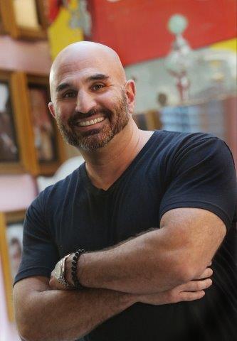 Smiling bald man with a beard in a black t-shirt crossing his arms.